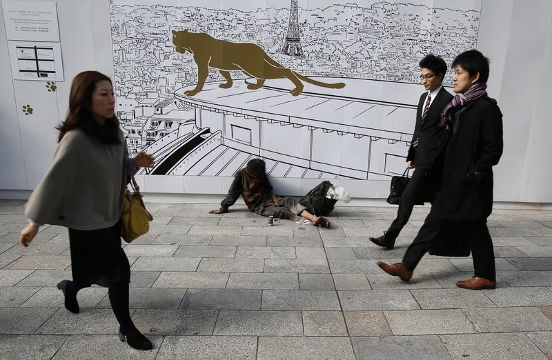 © Reuters. A man takes a nap along a street next to his belongings as pedestrians walk past at Tokyo's Ginza shopping district