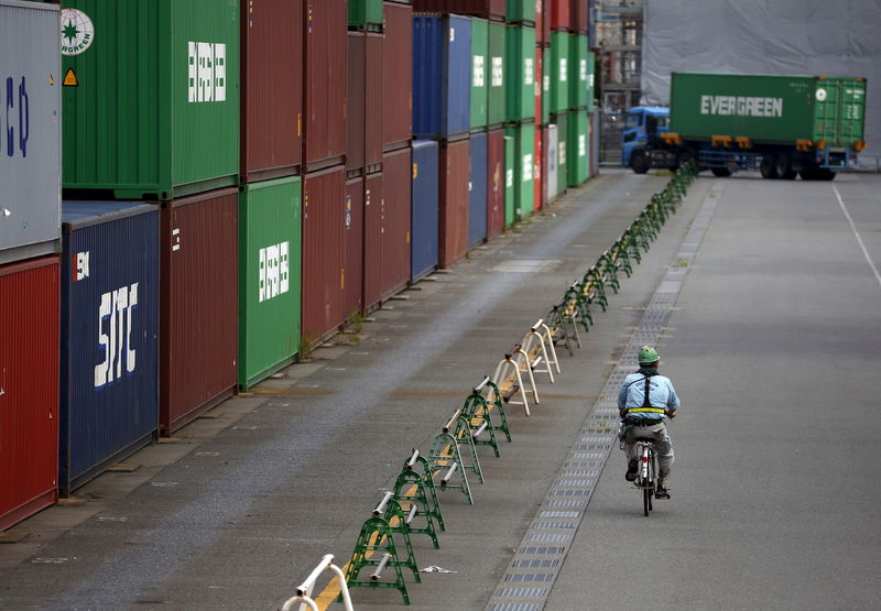 © Reuters. A worker rides a bicycle past containers at a port in Tokyo