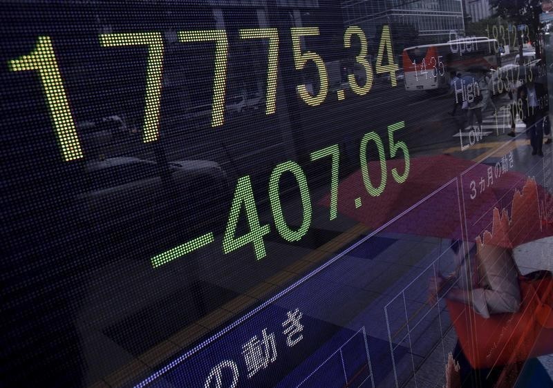 © Reuters. A pedestrian holding her umbrella is reflected on an electronic board showing the Japan's Nikkei average outside a brokerage in Tokyo