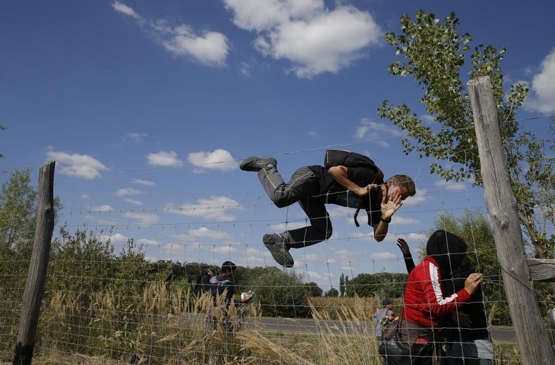 © Reuters. Migranti scavalcano una rete del centro di raccolta nei pressi di Roszke, in Ungheria 