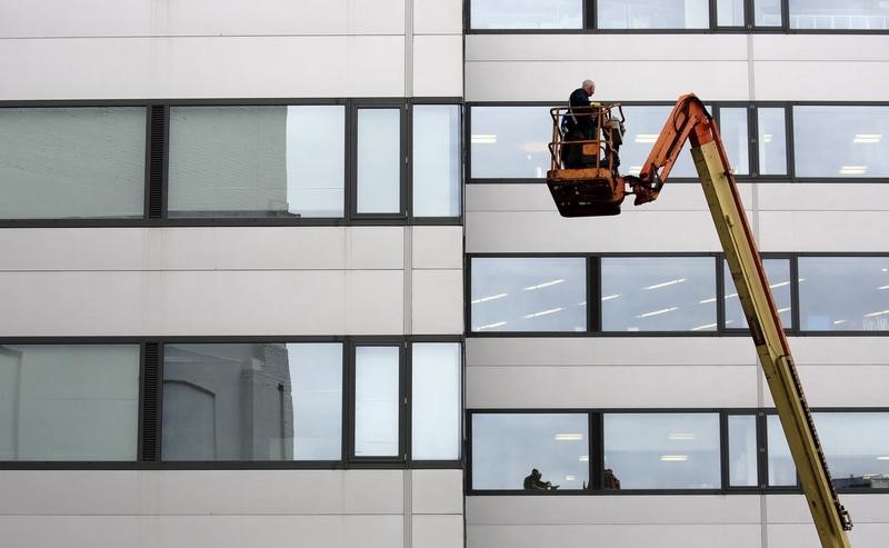 © Reuters. Workmen are seen on a crane near an office building in the financial district of London