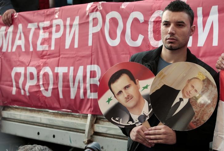 © Reuters. A participant hold images of Russian President Putin and Syrian President al-Assad during an anti-war protest organised by the Communist party near the U.S. embassy in Moscow