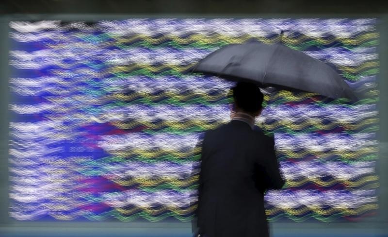 © Reuters. A woman holding an umbrella looks at an electronic stock quotation board outside a brokerage in Tokyo