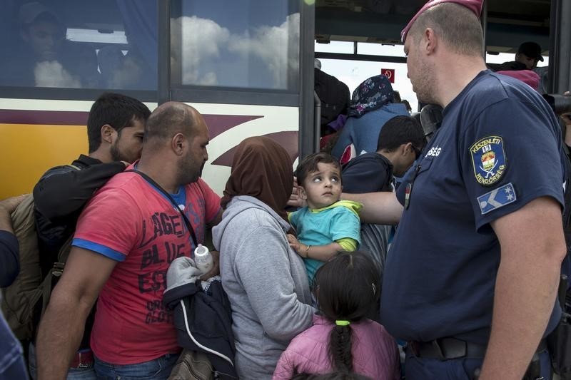 © Reuters. A child looks at a Hungarian police officer as migrants board a bus at a collection point in the village of Roszke