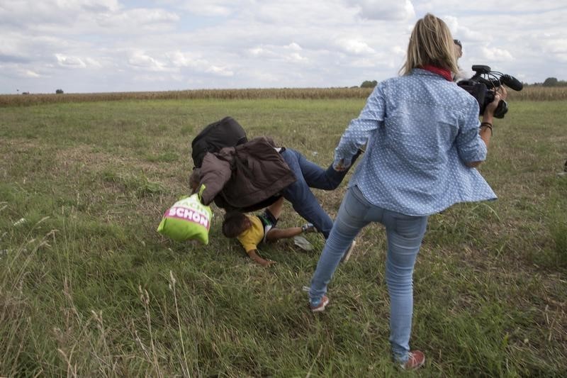 © Reuters. Imigrante com criança cai no chão após ser chutado pela cinegrafista húngara Petra Laszlo