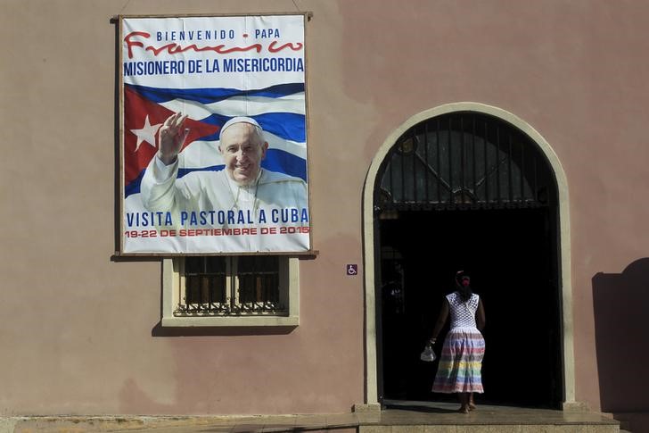 © Reuters. Mulher entra em igreja com cartaz anunciando a visita do papa Francisco a Cuba em Santiago de las Vegas, Cuba