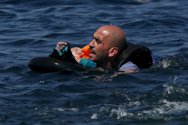 © Reuters. Syrian refugee holding a baby in a lifetube swims towards the shore after their dinghy deflated some 100m away before reaching the Greek island of Lesbos