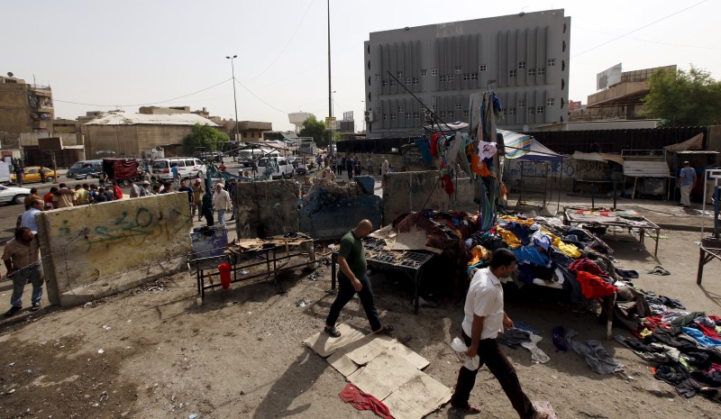 © Reuters. Men walk past the site of a suicide bomb attack in Baghdad