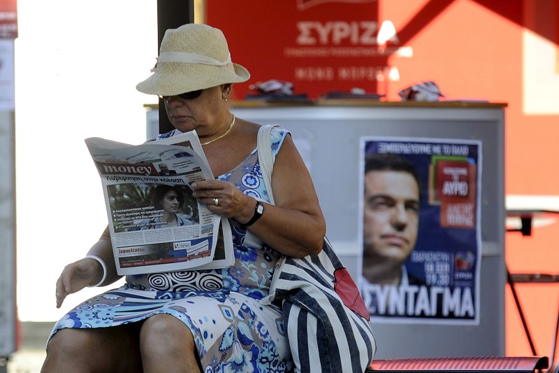 © Reuters. Mulher lê jornal em ponto de ônibus em frente a cartaz de campanha do ex-premiê grego Alexis Tsipras em Atenas