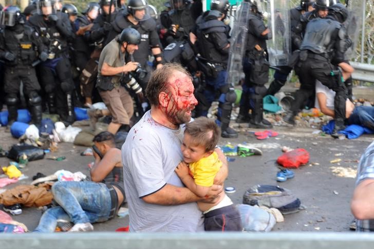 © Reuters. Imigrante ferido carrega criança durante confronto com polícia na fronteira da Hungria com a Sérvia