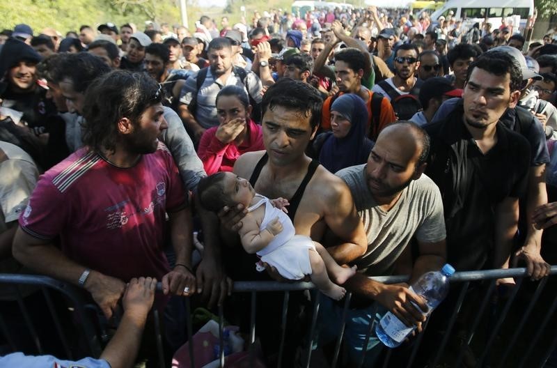 © Reuters. Un migrante tiene in braccio il suo bambino in attesa di salire su un pullman a Tovarnik, in Croazia