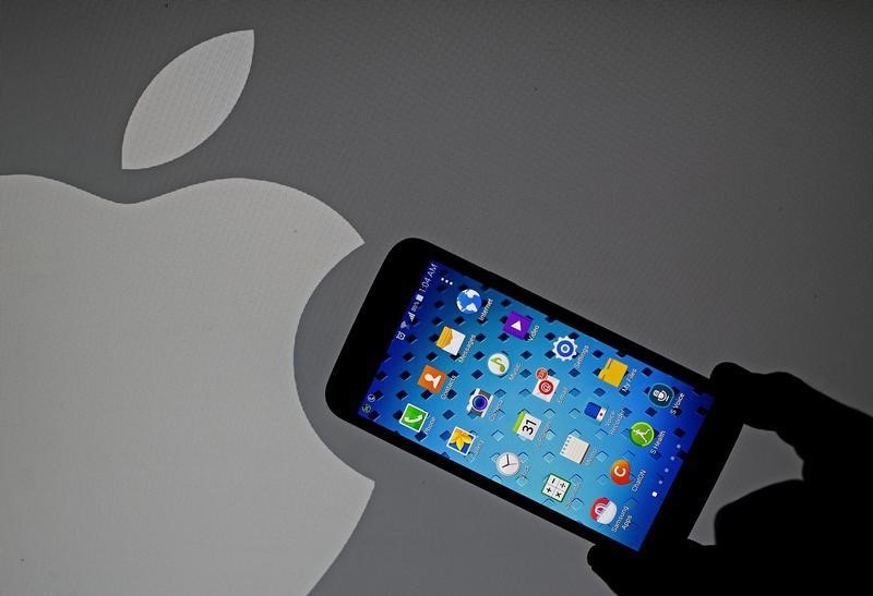 © Reuters. A Samsung Galaxy S5 smartphone is held next to a logo of Apple in this illustration photo in Sarajevo