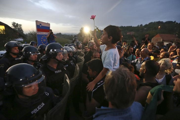 © Reuters. Criança segura flor em frente a policiais eslovenos na fronteira com a Croácia em Harmica