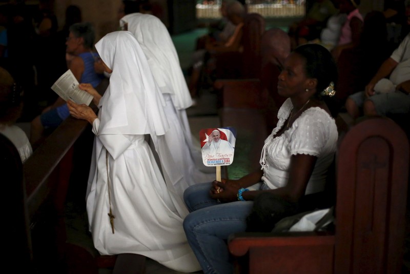 © Reuters. Woman holds a sign with an image of Pope Francis next to nuns during a mass celebrating the pope's visit, in the church of the Virgin of Charity of El Cobre in Havana