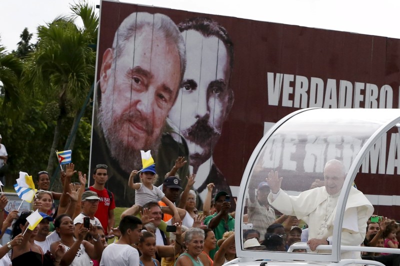 © Reuters. El Papa Francisco saluda a los creyentes mientras pasa en frente de vallas con las imágenes del ex presidente cubano Fidel Castro y del héroe de la independencia de Cuba José Martín, a las afueras del aeropuerto de La Habana