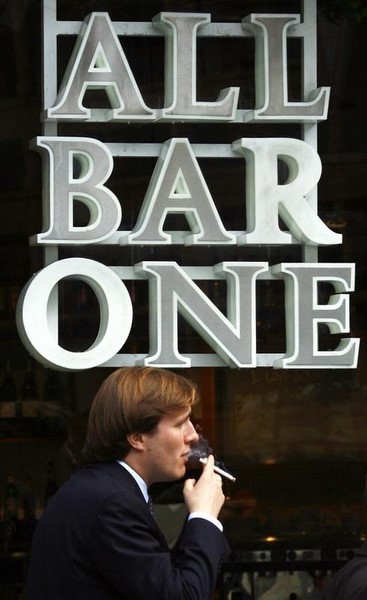 © Reuters. Man smokes in front of All Bar One pub in London