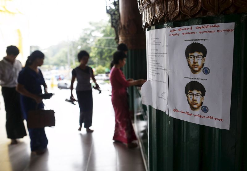 © Reuters. People line up near wanted poster for main suspect of deadly bomb blast in Bangkok, put up by local authorities at Shwedagon pagoda in Yangon, Myanmar