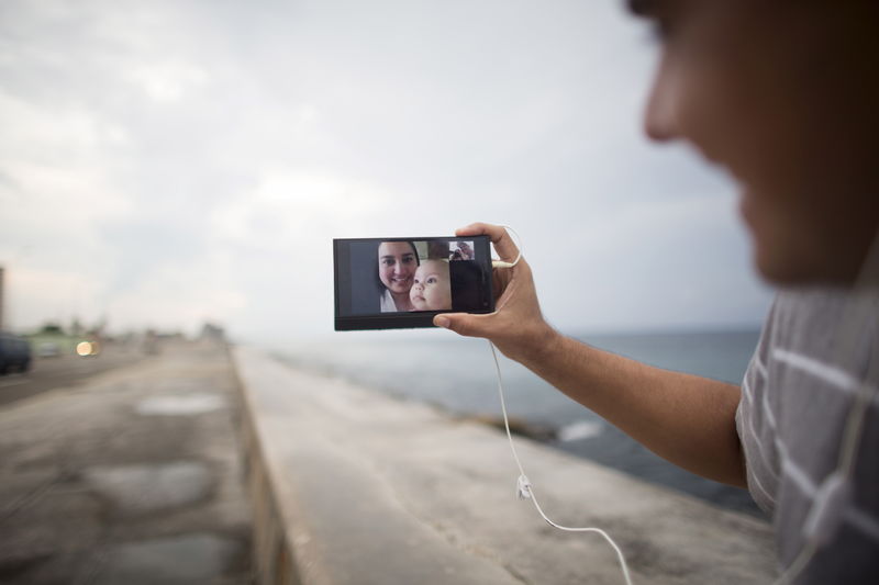 © Reuters. Artist Dariel Llerandis, 31, shows his wife and his 6 month old daughter who live in Miami as he speaks to them using the internet at a Wi-Fi hotspot in Havana