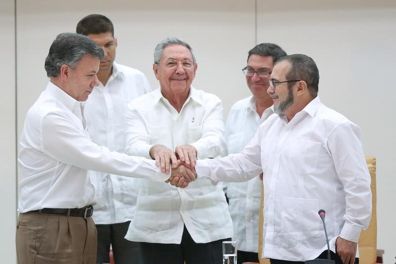 © Reuters. El presidente cubano Raúl Castro (al centro) de pie mientras el presidente de Colombia Juan Manuel Santos (izq) y el líder de las FARC Rodrigo Londoño "Timochenko" estrechan manos tras la firma de un acuerdo en La Habana