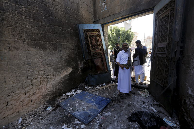 © Reuters. People stand at the gate of the al-Balili mosque after two bombings hit the mosque in Yemen's capital Sanaa