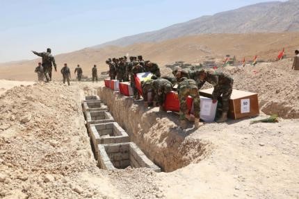 © Reuters. Kurdish peshmerga forces carry coffins containing the remains of Yazidis during a burial ceremony at Mazar Sharaf al-Din