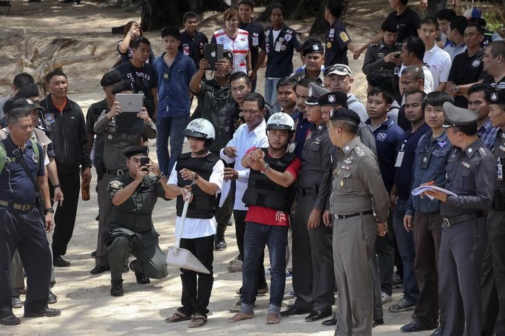 © Reuters. Two workers from Myanmar, suspected of killing two British tourists on the island of Koh Tao last month, stand near Thai police officers during a re-enactment of the alleged crime, on the island