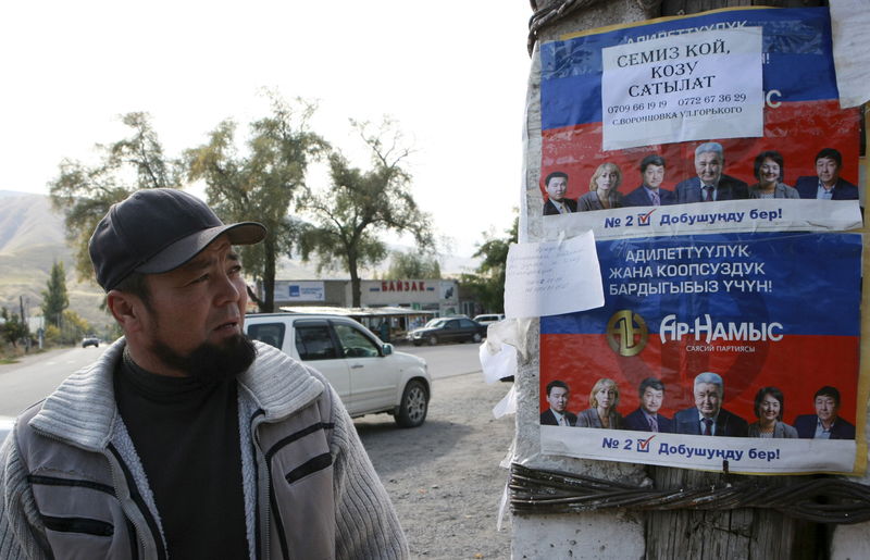 © Reuters. A local resident looks at election campaign posters, which are on display in the village of Vorontsovka near the capital Bishkek