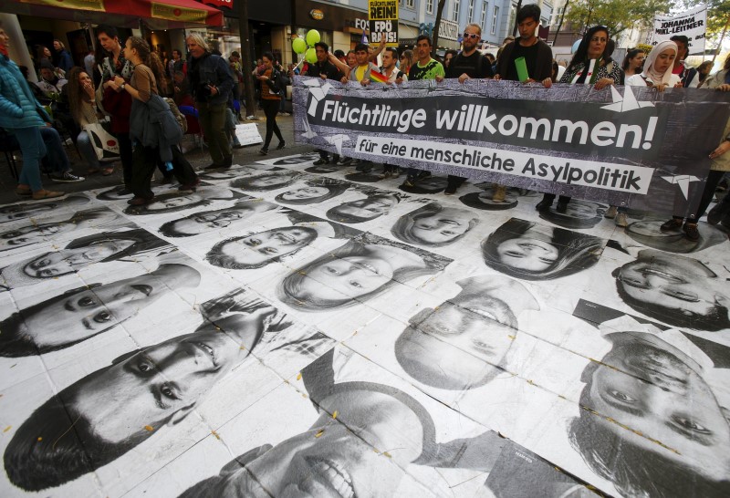 © Reuters. Protesters march over portraits of refugees, laid out as an arts project, during a demonstration in support of refugees in Vienna