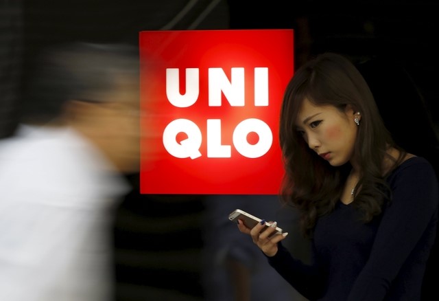© Reuters. File photo of a woman holding her mobile phone standing next to a logo of Fast Retailing's Uniqlo outside its store in Tokyo