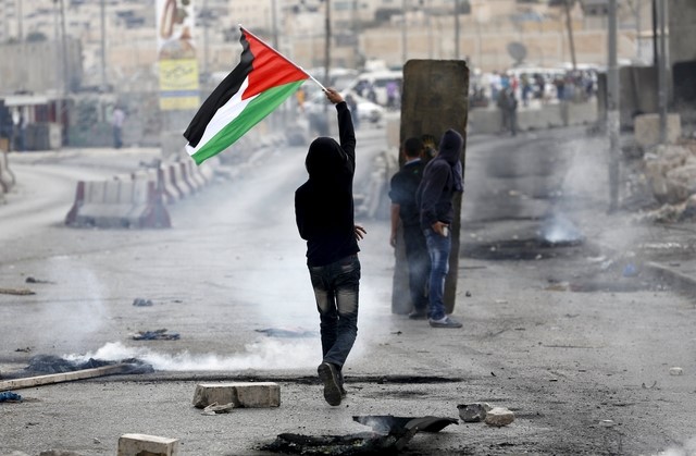 © Reuters. Palestinian protester holds a Palestinian flag as others take cover during clashes with the Israeli army at Qalandia checkpoint near occupied West Bank city of Ramallah