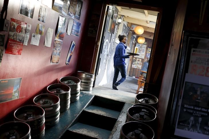 © Reuters. A woman carries beer produced by brewing company SAB Miller past kegs at a bar in Cape Town