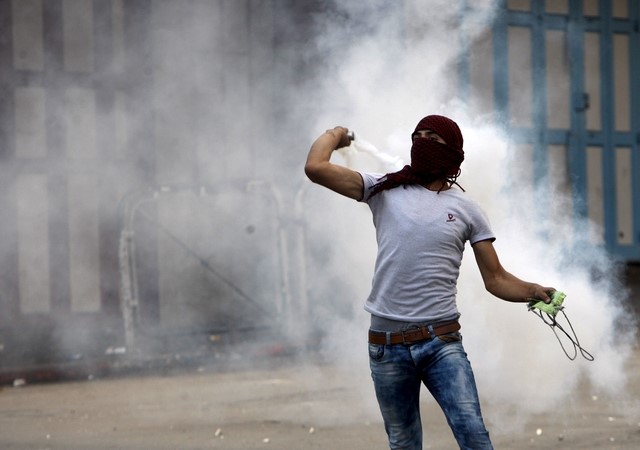 © Reuters. Manifestante palestino atirando gás em tropas israelenses durante confronto na cidade de Hebron, na Cisjordânia