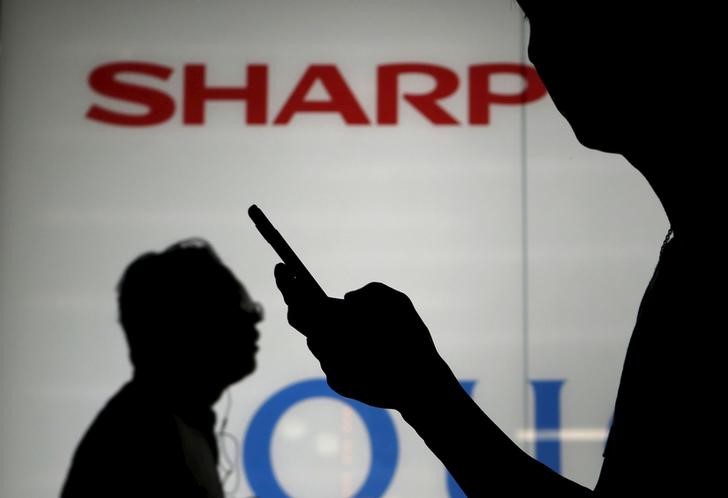 © Reuters. A man using his mobile phone walks past a logo of Sharp Corp outside an electronics shop in Tokyo