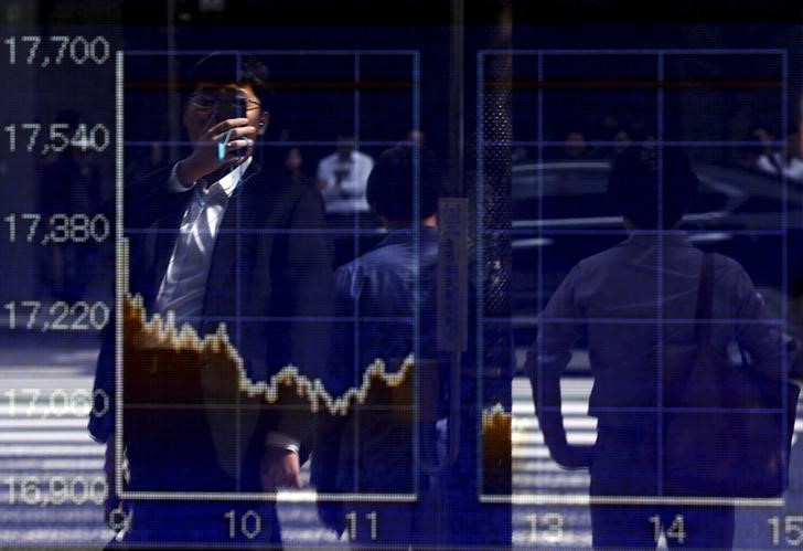 © Reuters. A man using a smartphone is reflected on a graph showing today's movements of Nikkei share average outside a brokerage in Tokyo