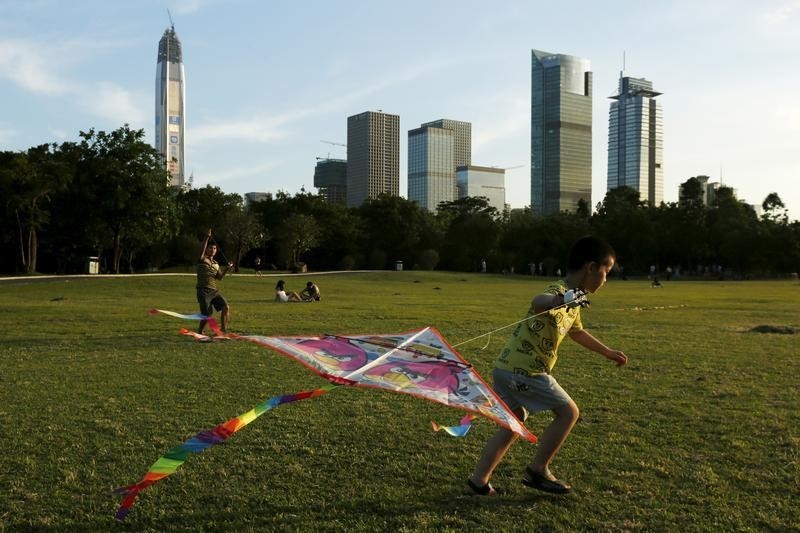 © Reuters. People fly kites at a park in front of commercial towers in Shenzhen