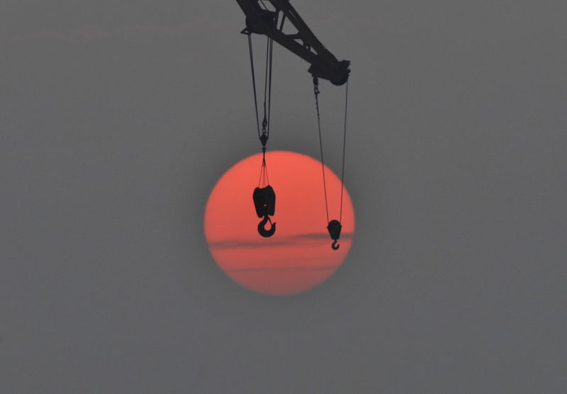 © Reuters. The hooks of a crane are pictured in front of the setting sun in Qingdao