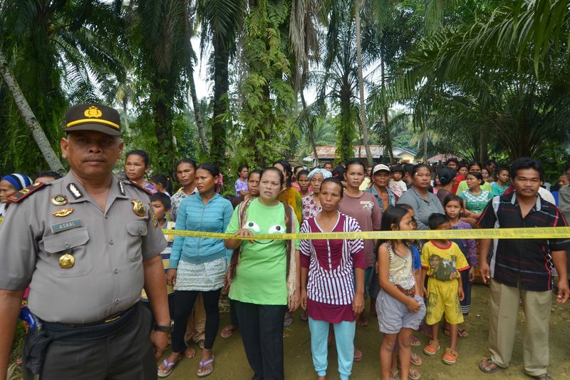 © Reuters. Residents look on as a policeman stands guard in Suka Makmur village in Singkil district, Indonesia Aceh province