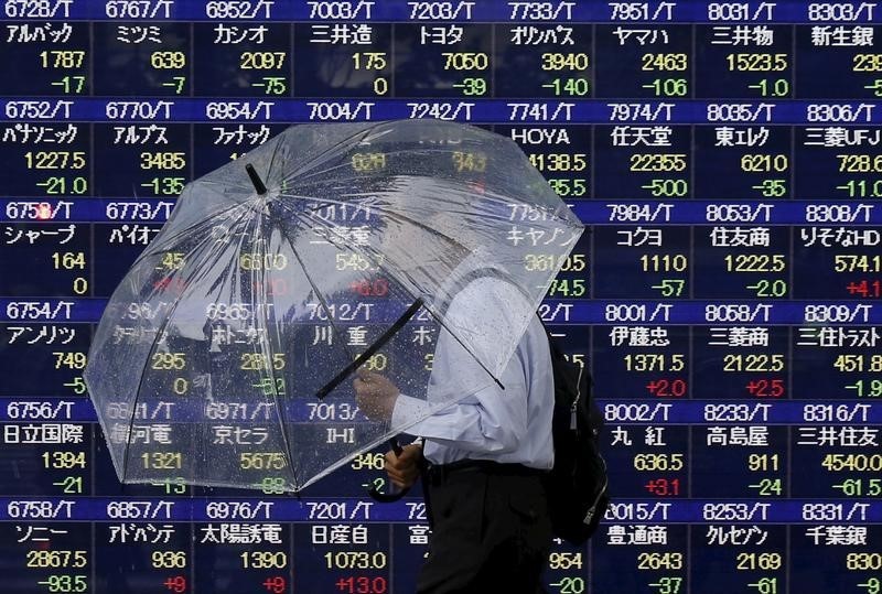 © Reuters. A man holding an umbrella walks in front of an electronic stock quotation board outside a brokerage in Tokyo