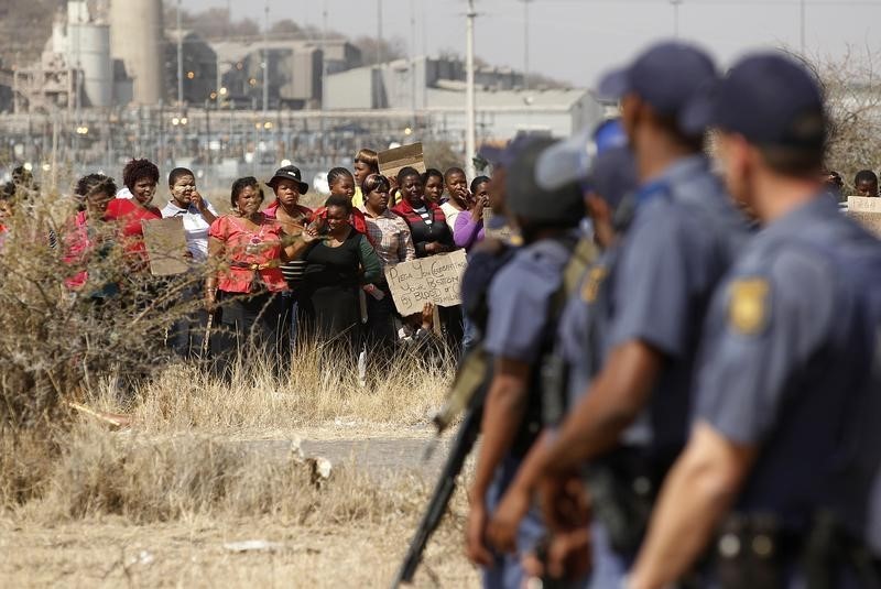 © Reuters. Police look on as women carry placards in protest against the killing of miners by the South African police on Thursday, outside a South African mine in Rustenburg