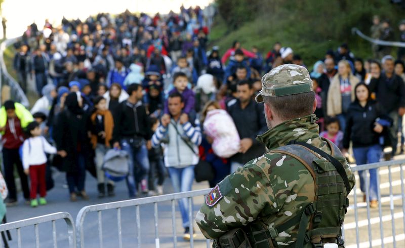 © Reuters. Un miembro del Ejército esloveno observa a los inmigrantes caminando hacia la frontera austriaca cerca de la localidad de Sentilj, en Eslovenia.