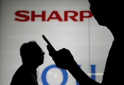 © Reuters. File photo of a man using his mobile phone walking past a logo of Sharp Corp outside an electronics shop in Tokyo