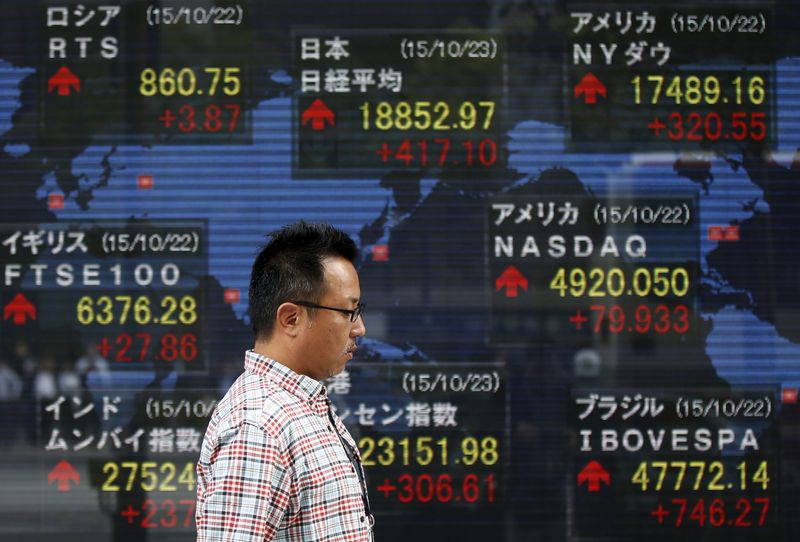 © Reuters. A man walks past an electronic board showing the stock market indices of various countries outside a brokerage in Tokyo