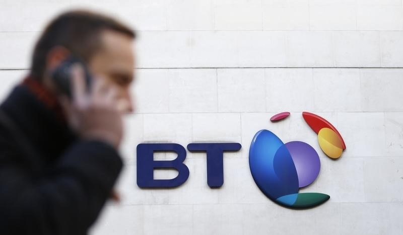 © Reuters. A man talks on his mobile phone as he walks past a BT logo in London
