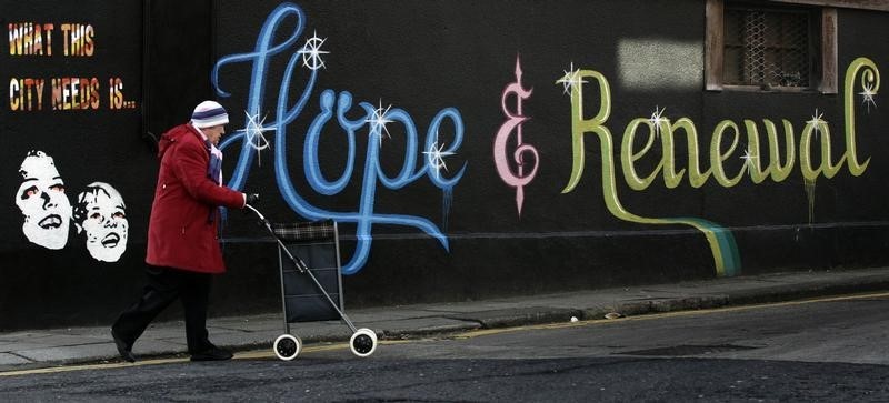 © Reuters. A woman pushes her shopping trolley past graffiti on the side of a building in Dublin