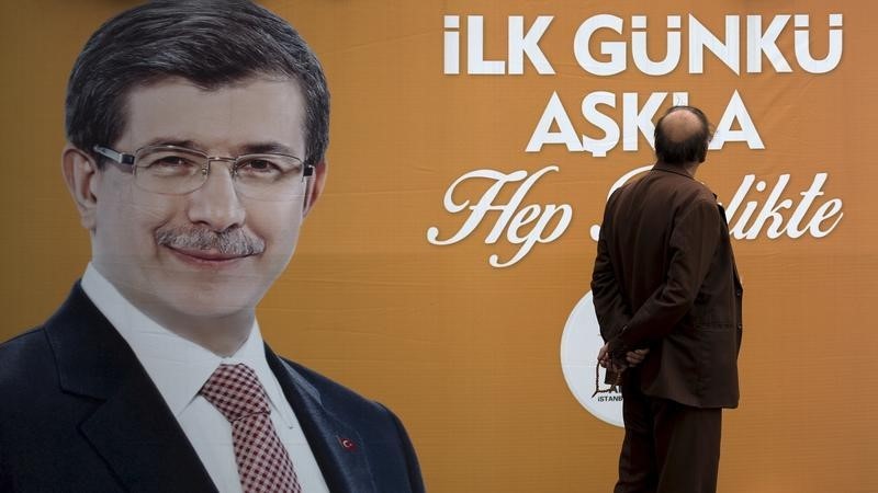 © Reuters. Man looks at an election poster of the ruling AK Party that features a picture of Turkey's Prime Minister Davutoglu on it in Istanbul