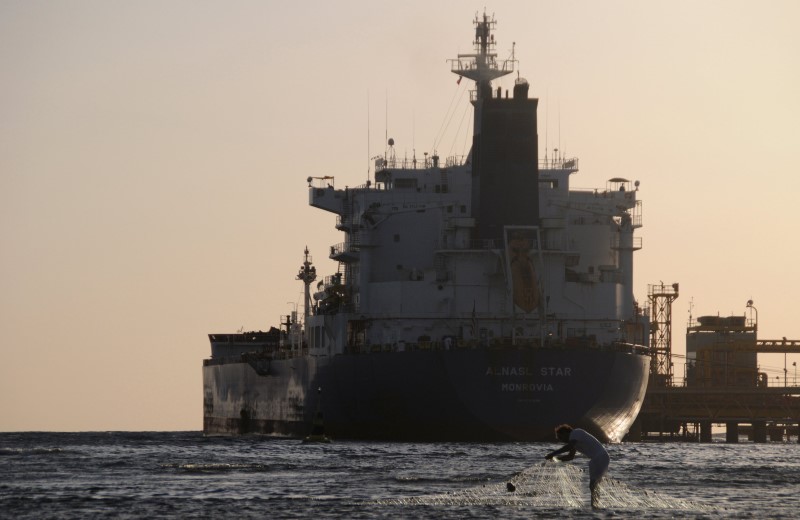 © Reuters. File photo of fisherman pulling in his net as an oil tanker is seen at the port in the northwestern city of Duba