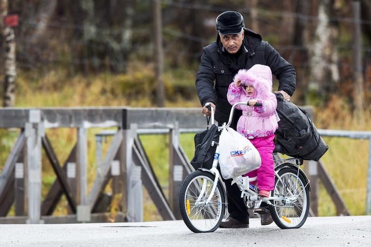© Reuters. Man pushes a girl across the border from Russia to Norway on a bicycle with flat tyres at the Storskog border station in northern Norway