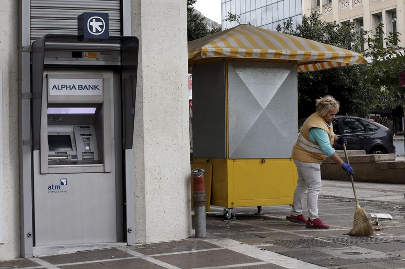 © Reuters. A woman cleans the pavement in front at an ATM outside an Alpha Bank branch in Athen