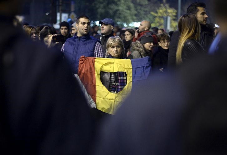 © Reuters. Manifestante segura bandeira romena em frente a policiais durante protesto pela renúncia do governo da Romênia após o número de mortos em um incêndio numa boate em Bucareste chegar a 32