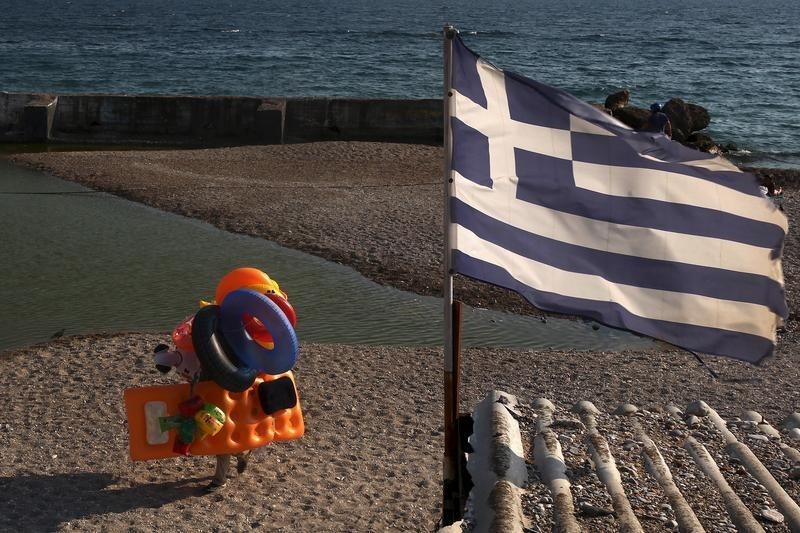 © Reuters. A beach vendor walks on the beach while a Greek flag flutters at a southern Athens suburb